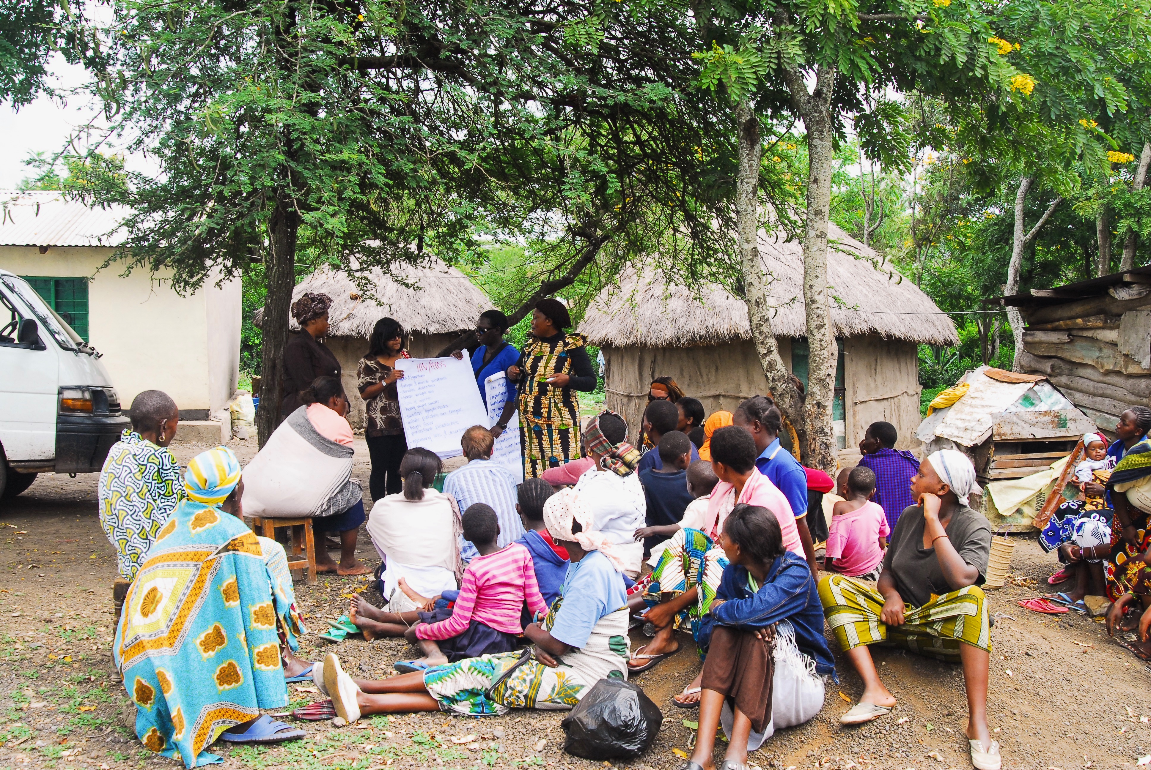 A group of people gather around a tree. They are watching the woman at the front who is writing in flip chart paper